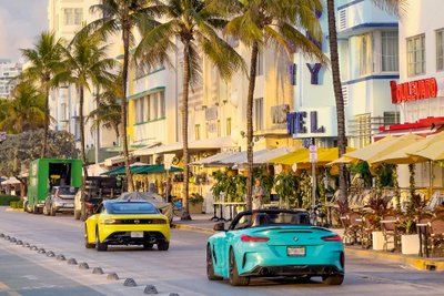 SPortwagen fahren eine Straße mit Palmen und Restaurants entlang.