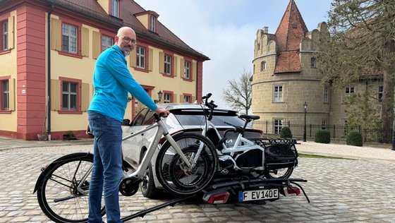 Mann schiebt ein Fahrrad auf einen Fahrradträger. 