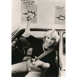 Ein historisches Plakat einer Aufklärungskampagne zeigt eine Frau mit Sicherheitsgurt im Auto. 