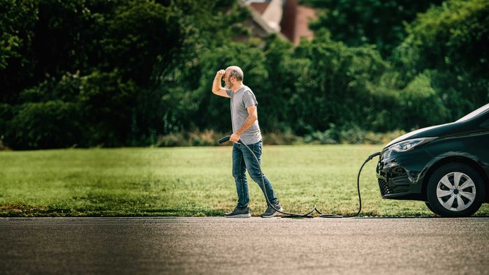 Mann hält Kabel von E-Auto in der Hand. 