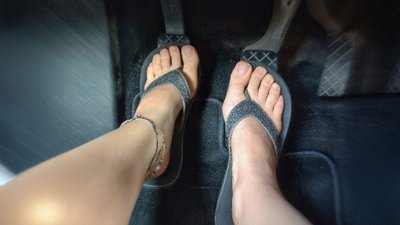 Füße mit Flipflops an den Pedalen eines Autos.
