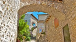 Verwinkelte Dorfgasse mit Steinhäusern, Torbögen und Pflanzen.