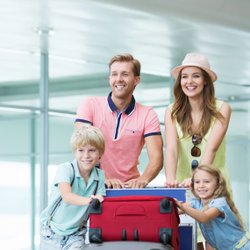 Junge Familie schiebt Gepäckwagen mit Koffern durch Flughafen.