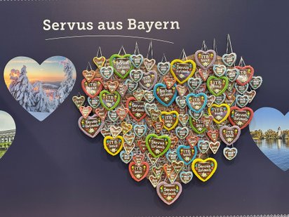 Bunte Lebkuchenherzen hängen an einer Wand mit dem Schriftzug „Servus aus Bayern.