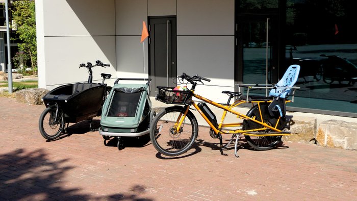 Verschiedene Fahrradanhänger für den Kindertransport stehen vor einem Gebäude.