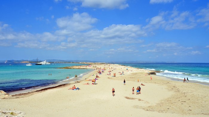Blick auf eine Landzunge mit Sandstrand umgeben von türkisblauem Wasser.