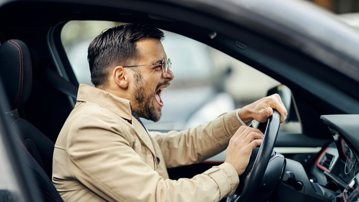 Wütender Mann sitzt im Auto und drückt auf die Hupe. 