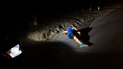 Mann liegt im Dunklen vor einem Auto. 