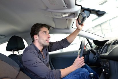 Mann stellt sich im Auto den Rückspiegel ein.