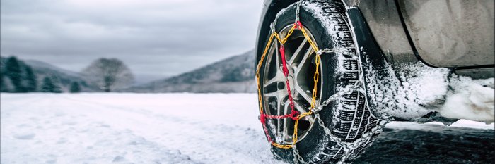 Autoreifen in Schneeketten auf verschneiter Straße.