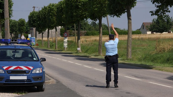 Französischer Polizist steht auf der Straße und hält ein Auto an. 
