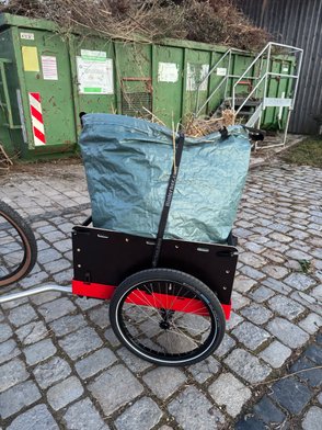 Ein Sack mit Gartenabfällen auf dem Fahrradanhänger Hmax light von Hinterher vor einem Gartenabfällecontainer