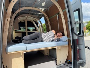 Eine Frau liegt auf dem Daybed des Moby Camper. 