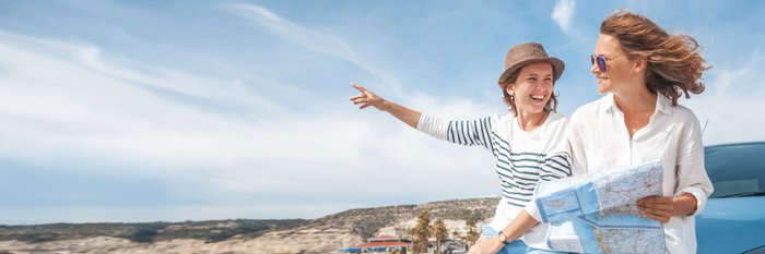 Zwei Urlauberinnen lehnen an Auto, bewundern Umgebung.