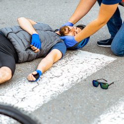 Ersthelfer versorgt verletzten Radfahrer nach Verkehrsunfall. 