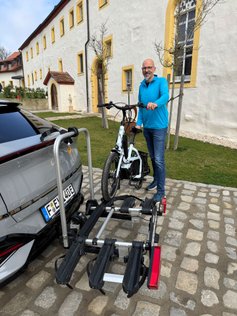 Mann schiebt Fahrrad auf einen Fahrradträger. 