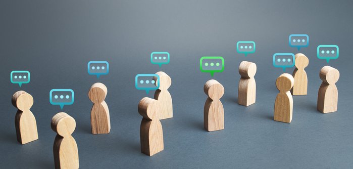 Mehrere Holzfiguren mit unterschiedlich farbigen Sprechblasen