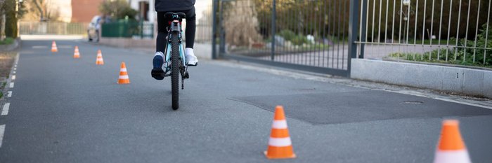 Ein junge Fahrradfahrerin fährt einen Parcours markiert mit rot-weißen Hütchen. 