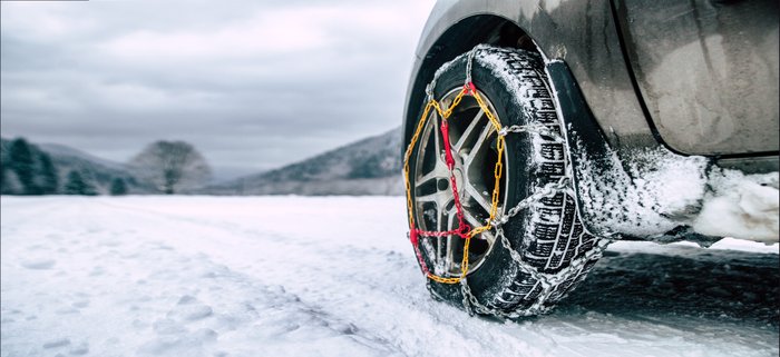 Autoreifen in Schneeketten auf verschneiter Straße.