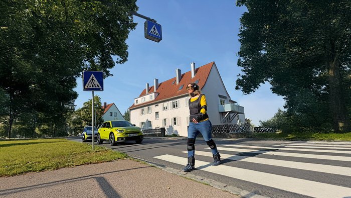 Eine Fußgängerin überquert im Altersanzug einen Zebrastreifen.