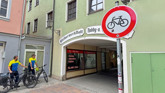 Zwei Polizisten stehen an einem Durchgang und kontrollieren Radfahrer. 