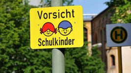 Kinder warten an der Straße, ein Auto biegt ab. 