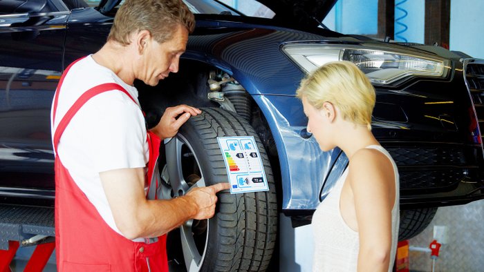 Ein Mechaniker zeigt einer Kunding das neue Reifenlabel an einem Reifen.
