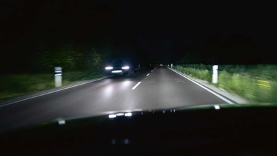 Eine dunkle Fahrbahn mit entgegenkommenden Auto, welche beleuchtet wird.