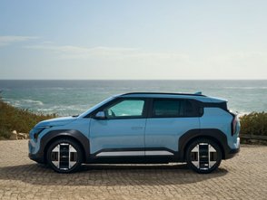 Blauer Kia EV3 steht auf einem Platz am Meer. Zu sehen ist die Seite. 
