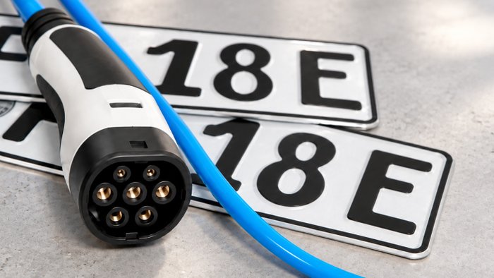 Zwei Kennzeichen eines E-Autos liegen auf dem Boden mit einem Elektrostecker. 