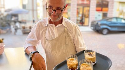 Kellner präsentiert Tablett mit drei kalten Kaffee-Kreationen.