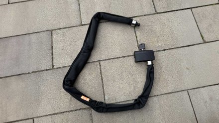 Das Falt- und Kettenschloss AXA Foldable 8-130 liegt auf dem Boden.