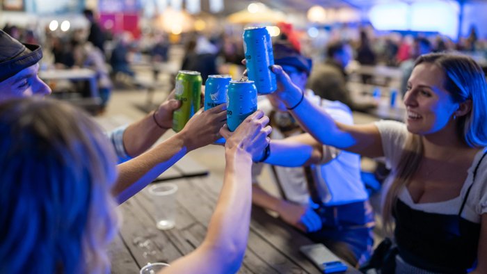 Fünf feiernde Festbesucher stoßen an einem Tisch mit Dosenbier an.