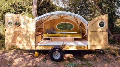 Roomy-Wohnwagen mit geöffneten Türen steht in einem Wald.