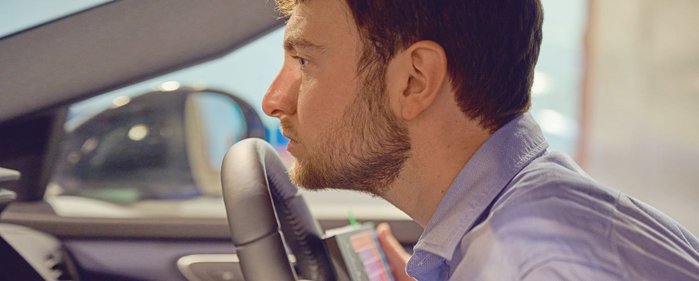 Ein Mann sitzt im Auto und riecht am Lenkrad.