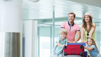 Junge Familie schiebt Gepäckwagen mit Koffern durch Flughafen.
