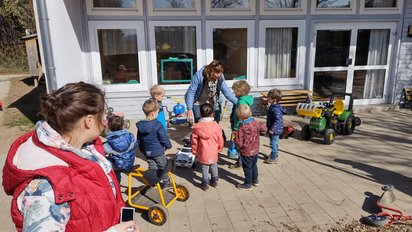 Kindergartenkinder mit Erziehern und Spielzeugfahrzeugen zu sehen.