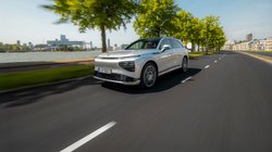 Ein E-Auto Xpeng G9 fährt auf einer Straße mit Bäumen an einem Fluss entlang.