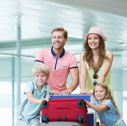 Junge Familie schiebt Gepäckwagen mit Koffern durch Flughafen.