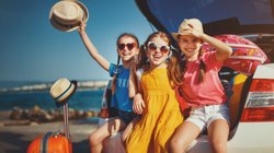 Drei Mädchen sitzen im Kofferraum und freuen sich auf den Urlaub. 