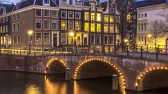 Blick auf einen Fluss in Amsterdam, im Hintergrund eine Brücke und Häuser.