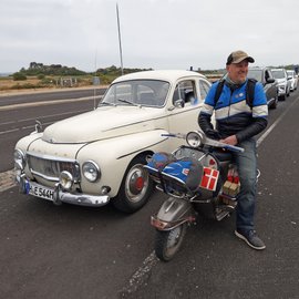 Mann mit Motorrad neben Volvo Oldtimer.