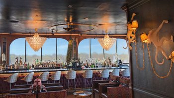 Blick in eine Bar mit Tresen, Barhockern und Panoramafenstern.