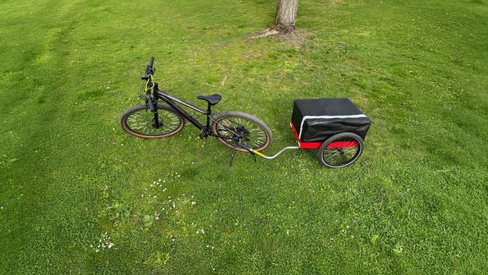 Der Fahrradanhänger Hinterher Hmax light mit der Falttasche auf einer Wiese mit Fahrrad 