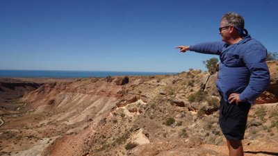 Ein Mann steht auf einer felsigen Anhöhe und zeigt auf das Meer.