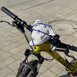 Eine Bäckertüte ist mit dem Lenkerspannband Carryyygum am Lenker eines Fahrrads befestigt.