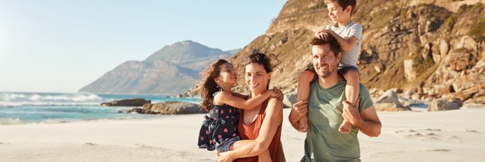 Ein junges Paar läuft mit seinen beiden Kindern am Strand einer Insel entlang.