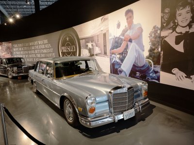 Schwarzer Mercedes-Benz 600 Pullmann und silberner Mercedes-Benz 600 Sedan in Ausstellung vor einem Foto mit Elvis.