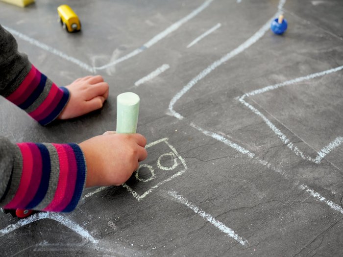 Ein Kind malt mit Kreide auf einer Straße.