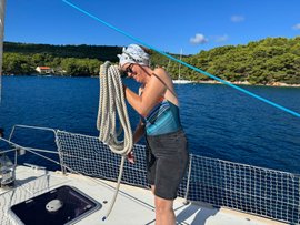 Eine Frau wickelt auf einer Segeljacht ein Seil auf.